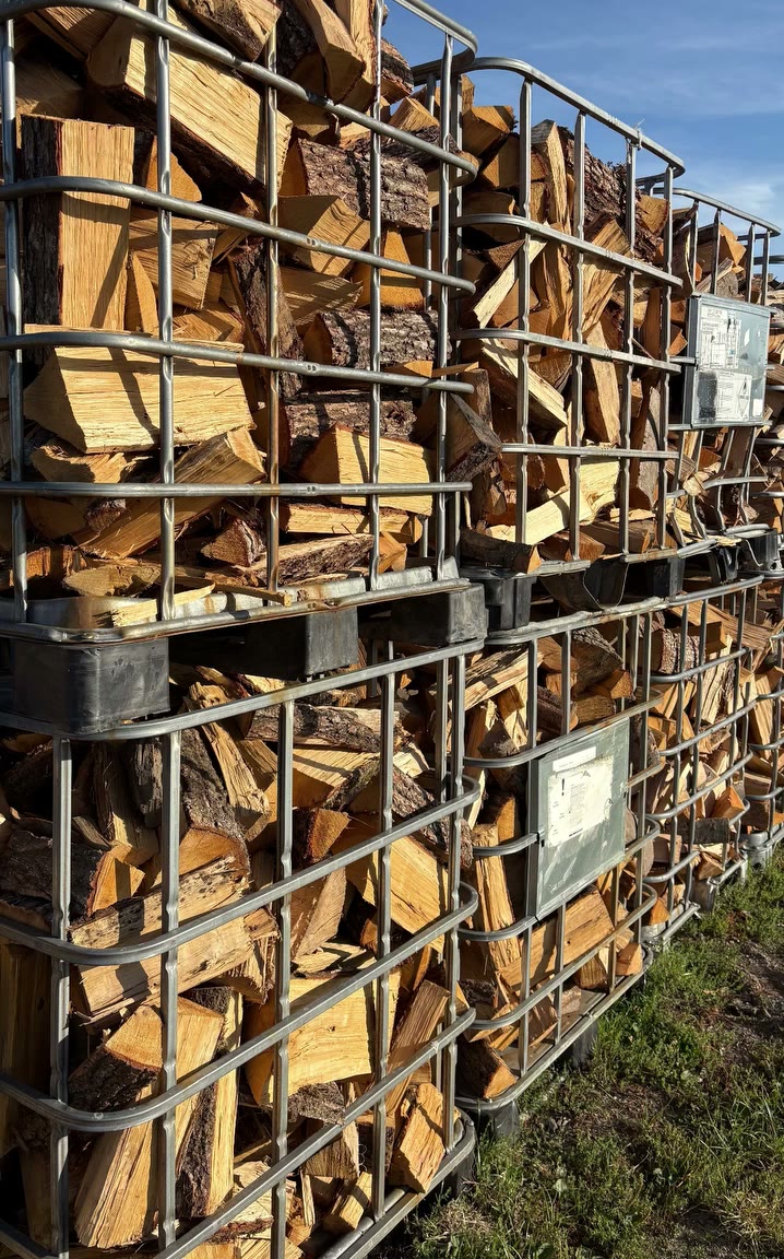 Mehrere Gitterboxen voll gespaltenem Brennholz in der Sonne